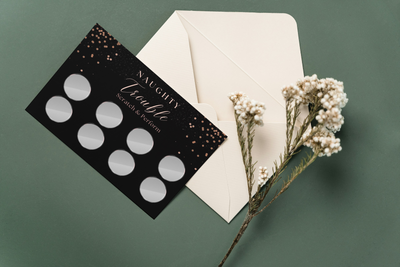Beautiful flat lay of Naughty Trouble scratch cards with whipped cream, cuffs, and chocolates for a sexy couples game night.