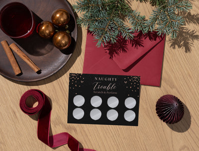 Naughty Trouble scratch cards laid out beside wine glasses and candles, setting the mood for a hot couple’s night in.
